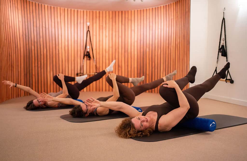 Groep vrouwen doet Pilates oefeningen op mat in studio.