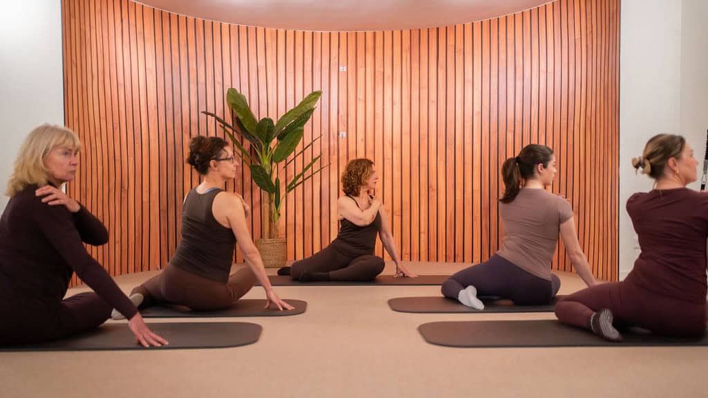 Vijf mensen doen yoga of stretching oefeningen in een studio met houten wand.