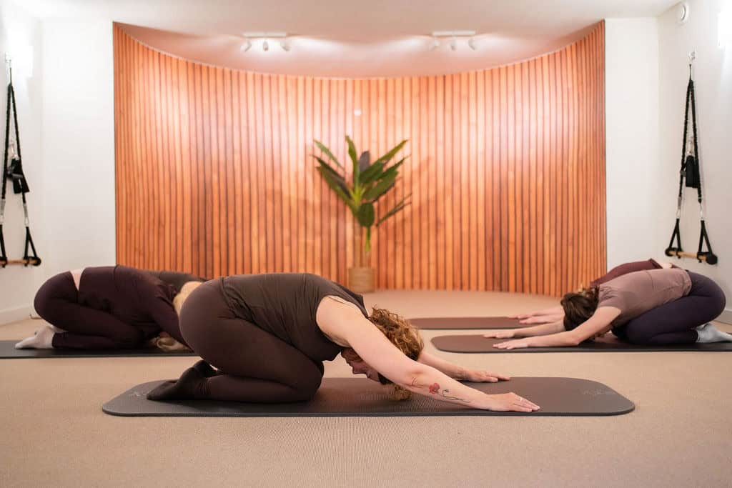 Mensen doen een yoga-achtige stretch in een rustige studio.