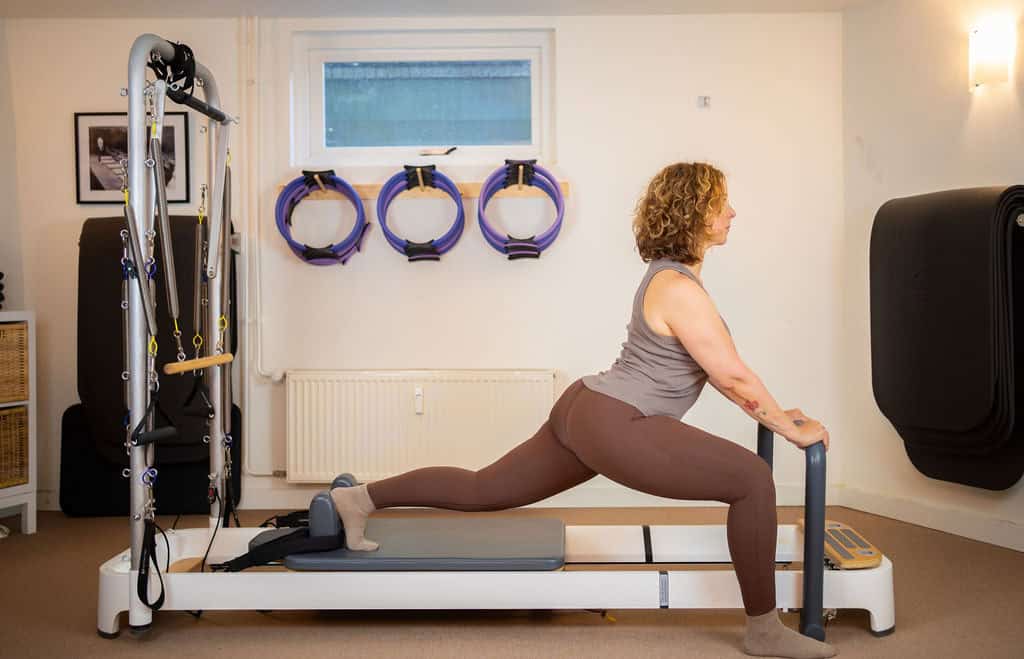 Vrouw doet Pilates op reformer bij Movement Studio, gericht op flexibiliteit en kracht.