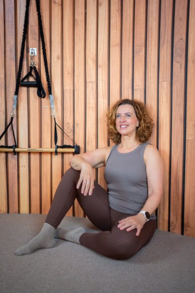 Vrouw in Pilates-omgeving met houten wand en trainingsbanden.