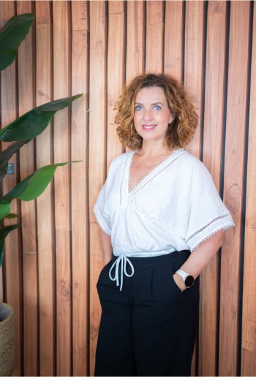 Vrouw met curly haar poseert in studio met houten achtergrond en groene plant.